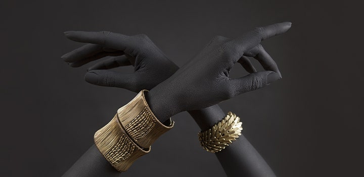 Grey photo of crossed hands with gold bracelets in color.