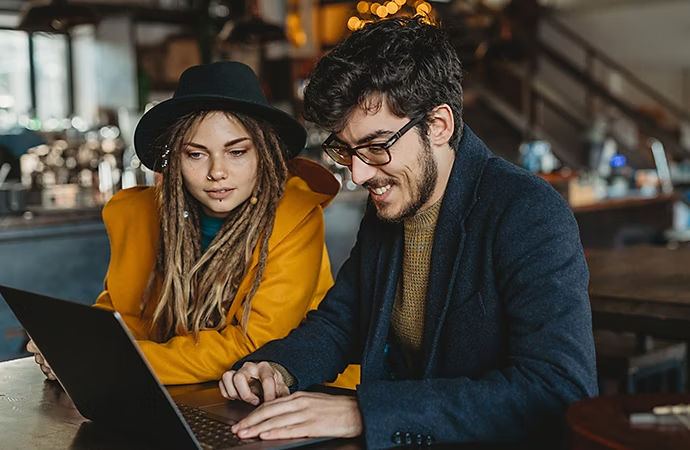 Two people reviewing a script together on a laptop while sitting at a table