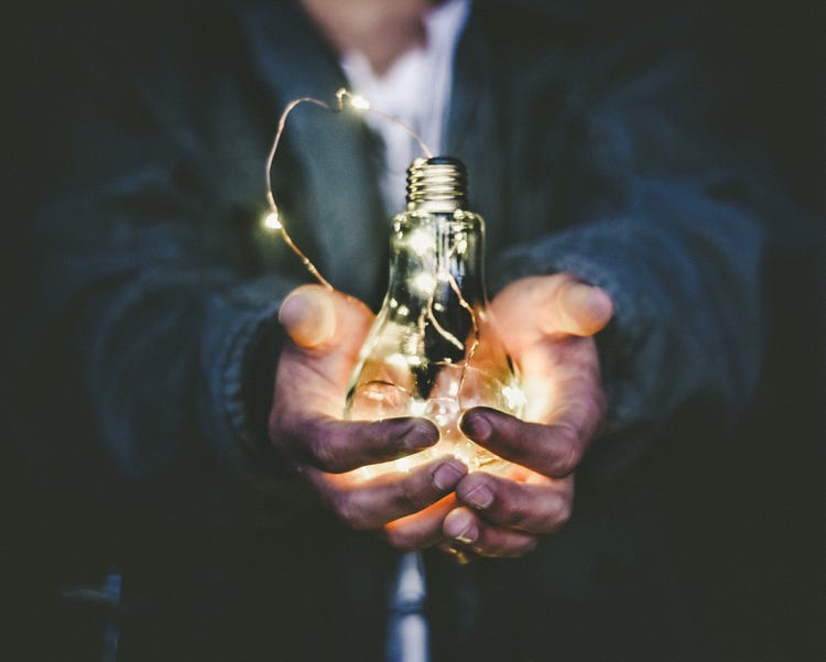 Outstretched hands holding a lightbulb with fairylights inside