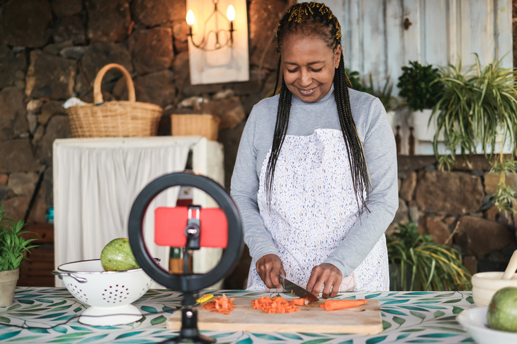 A content creator shooting a video of themselves cooking and chopping carrots using a phone and a ring light