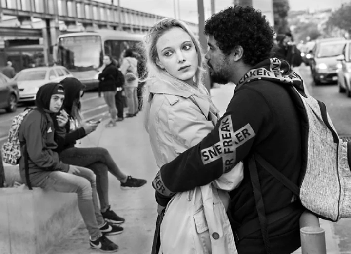 Photo of a couple embracing each other while waiting at bus stop on a street