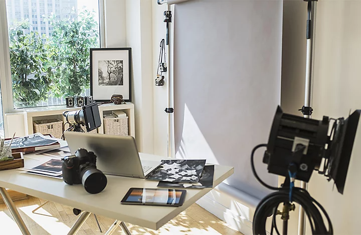 A photographer's working space, with a desk, laptop, and camera gear